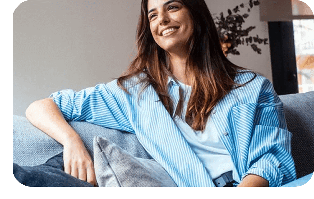 Group-1321316421-1 A woman sitting on top of a couch wearing a blue shirt.